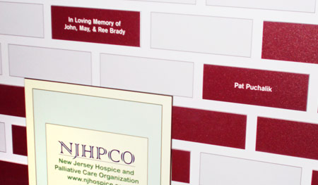 Four-foot tall, portable, wooden house display, crafted to fold for easy assembly and portability. Donor names are engraved on laminated engraving stock and applied to appear like bricks and roof tiles.