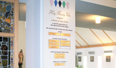 Corian plaque on an interior pillar at sanctuary entrance features etched and color-filled wording and engraved brass plates. Plaque is finished with stained glass "diamonds" to match altar's stained glass window.