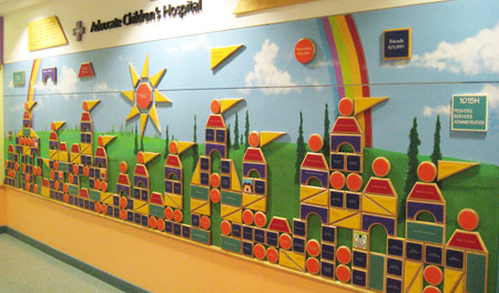 Wood shapes that mimic a child’s building blocks, form a castle over a hand-painted mural. Each piece has a colored personalized donor nameplate, representing a specific level of giving.