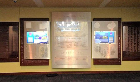 Dark cherry wood boards surround a silver, metal laminated center board. Donor names are printed on Lexan, sandwiched between acrylic panels. Wall includes dimensional lettering and two digital, touch-screen displays.