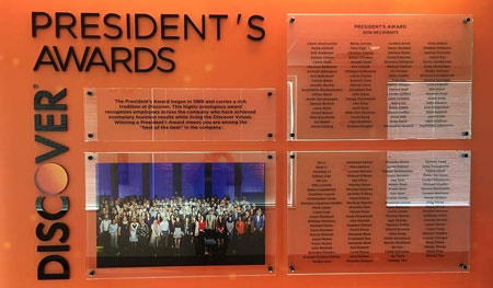 Floor to ceiling orange graphic, separates hall section from others. Top panel etched and color-filled in black. Remaining panels double glass plates, with awardee names printed on Lexan. Copy and logo are 1/2in. black acrylic.