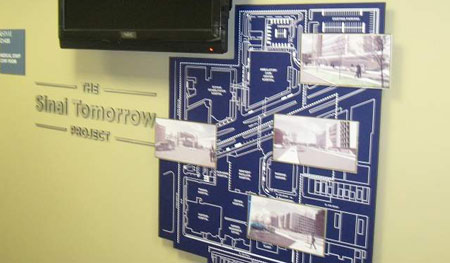 Wall is installed in a doctor's lounge and showcases a map of new hospital location and additions. Renderings are printed on metal and layered at the top. Digital display loops with donor information and project updates.