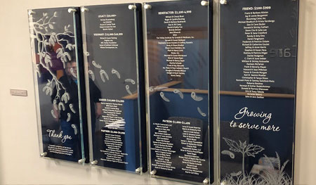 Engraved and paint filled acrylic panels with printed graphics and navy blue backs, attached with chrome plated standoffs, engraved copy denotes donor levels and names.