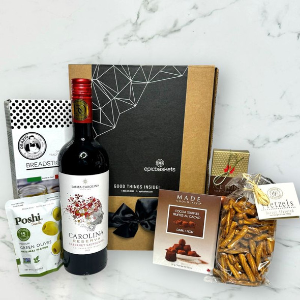 Cheers To You Gift Box with red wine, gourmet snacks, olives, crackers, and chocolate arranged in a gift basket