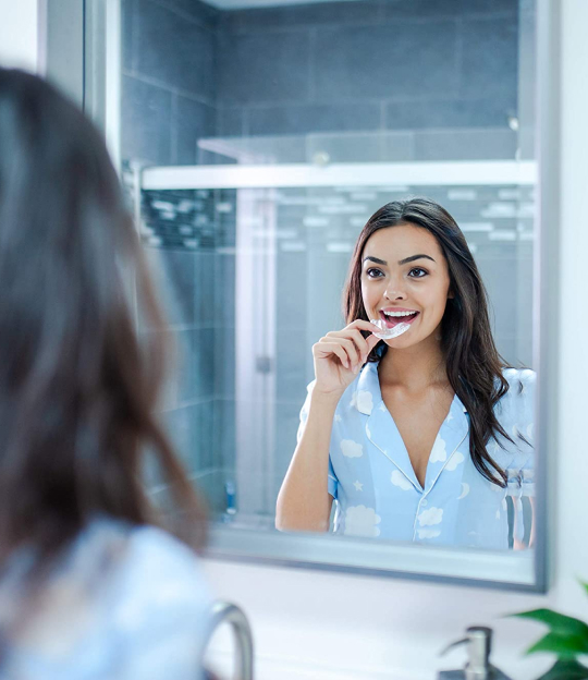 Woman putting on night guard in mirror