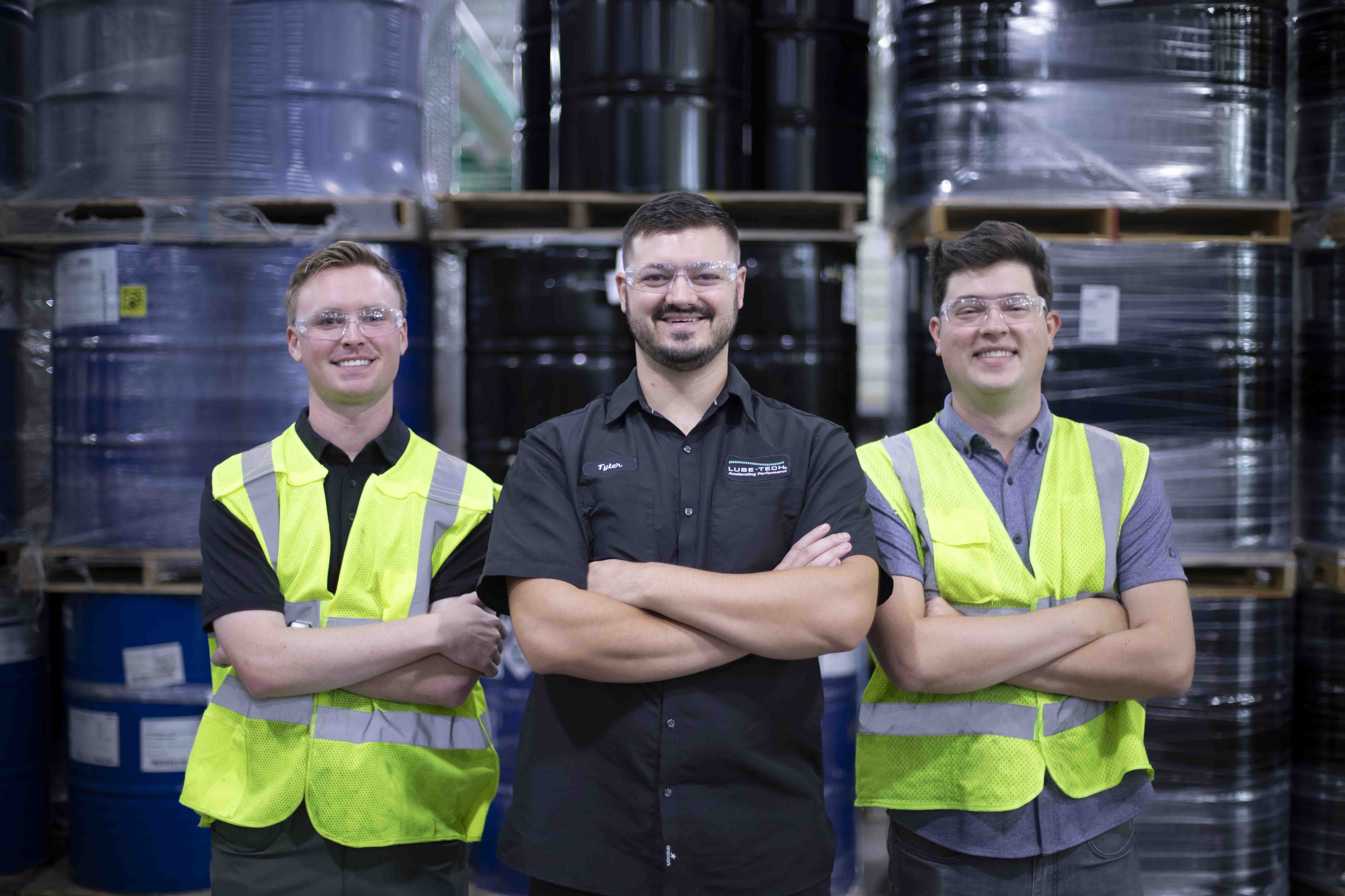 3 Reliable Plus employees standing in front of drums of chemicals