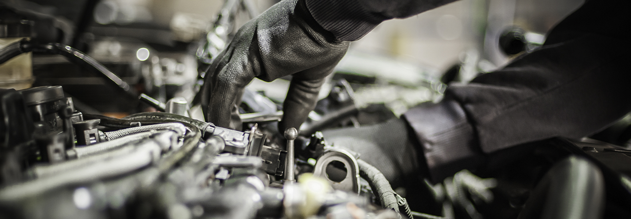 Hand wearing gloves working in a car's engine bay