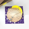 wooden sundial platform with black markings has yellow curved wall on purple square mat next to cardboard box