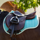 A close-up of a brown saddle with a teal quilted saddle pad on a horse, showcasing equestrian gear and natural surroundings.