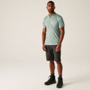 A full length view of a man wearing a blue/green polo shirt with black shorts.