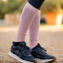 A close-up of a person's lower legs wearing pink compression sleeves and black athletic shoes on a gravel surface.