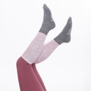 A pair of legs in playful pink patterned leg warmers and grey crew socks, playfully raised against a white background.