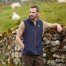 Man outdoors wearing a navy Ridgeline Kodiak fleece gilet with full-zip front, styled with a short-sleeve top and outdoor trousers.