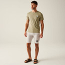 A full length view of a man wearing a sand-coloured t-shirt with shorts and sandals.