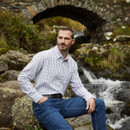 A man by a river wearing a navy check shirt
