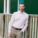 A man leaning against a fence wearing a rust coloured check shirt