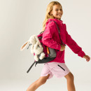 A smiling child in a bright pink jacket and shorts walks confidently with a backpack featuring a plush bunny. The scene conveys joy and adventure.