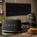 A sleek black Smeg toaster and kettle on a modern kitchen counter, with slices of toasted bread nearby.