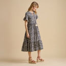 A woman poses in a stylish navy patterned dress with a flowing skirt and ruffled sleeves, paired with wedge sandals.