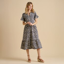 A woman poses in a patterned midi dress with short sleeves and a tiered skirt, paired with stylish wedge sandals against a neutral background.