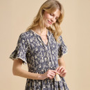 A woman wears a navy blue dress featuring an arrow pattern, with short ruffled sleeves and a tassel detail at the waist.