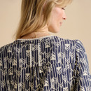Back view of a patterned shirt featuring geometric arrow designs in navy and cream, with decorative buttons and pleats.