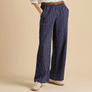 A person in navy pleated wide-leg pants, styled with a braided belt, white blouse, and light sneakers against a neutral background.