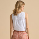 A person wearing a white sleeveless top with a lace back detail, paired with red and white striped pants, against a beige background.