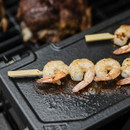 Grilled shrimp skewers sizzle on a black cooking surface, showcasing seasoned prawns with a golden-brown crust.