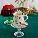 A view of a white mug with multicoloured polka dots on a cake stand