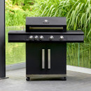 Black four-burner barbecue with closed hood, wide side shelves and cupboard storage, shown outdoors by water and greenery.