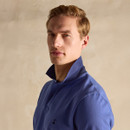 A man wearing a blue polo shirt with a collar, set against a neutral textured background.