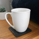 A white mug with a ribbed design positioned on a coaster.