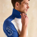 A man wearing a blue and white polo shirt with a large number 3 on the sleeve, adjusting his collar against a neutral background.