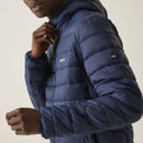 A person stands in a neutral pose, wearing a navy puffer jacket, white t-shirt, and dark trousers. The background is plain and light, evoking a casual vibe.