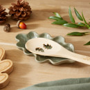 A view of a green Cooksmart Forest Fable leaf shaped spoon rest with a spoon on it on a wooden table