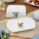 A butter dish with a cow illustration and a rectangular base featuring a calf design, both set on a textured tablecloth.