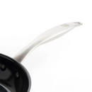 Close-up of a sleek stainless steel frying pan handle with a black non-stick surface, emphasizing its modern design.