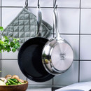 Two frying pans, one stainless steel and one non-stick, hang above a wooden bowl of vegetables, with a grey pot holder in the background.