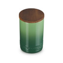 A green stoneware storage jar with a wooden lid and Le Creuset branding.