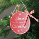 A view of a circle wooden red sign that says 'Believe in the magic of Christmas' hanging on a Christmas tree