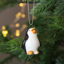 A view of a ceramic penguin hanging decoration hanging on a Christmas tree