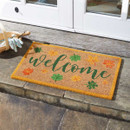 A colourful doormat with "Welcome" text surrounded by autumn leaves in green, orange, and yellow, placed at a doorway.
