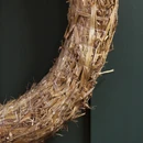 Detailed close-up of a straw wreath base, highlighting the overlapping golden straw fibres, loose strands and fine white thread holding the circular frame together.