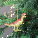 A glittery gold and red dinosaur ornament, suspended by a golden string hanging on a Christmas tree