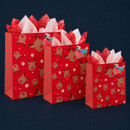 Three red Christmas gift bags in assorted sizes, featuring playful reindeer faces, snowflakes, striped sides and festive tissue paper.