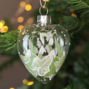 A close up view of a clear glass heart shaped hanging decoration with glittery snowdrop and ivy detailing hanging on a Christmas tree
