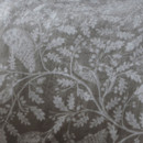 Close-up of beige fleece bedding showing white bird and oak leaf pattern in a soft velvety texture.