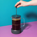 Someone lifting the plunger on the cafetière filled with coffee.