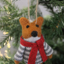 A felt ornament of a fox in a grey jumper and red scarf hangs on a Christmas tree with soft, glowing lights in the background. Cosy and festive.